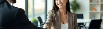 Eine asiatische Geschäftsfrau und ein Geschäftsmann schütteln sich in einem modernen Büro die Hand, symbolisieren Vertrauen und professionelle Partnerschaft.